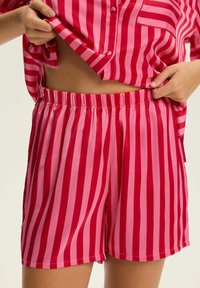 Różowy pasiaste piżama składająca się z bluzki z krótkim rękawem i dopasowanych szortów. Materiał jest gładki i błyszczący, z naprzemiennymi jasnoróżowymi i ciemnoróżowymi paskami.
