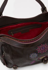 Brun läder axelväska med röd tygfodring. Har färgglada broderade blommönster och en dragkedjeficka inuti. Metallisk hårdvara.
