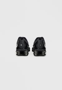 Čierne športové topánky s lesklým povrchom, vybavené polstrovaným golierom, textúrovanou zadnou časťou a zakrivenou podrážkou pre odpruženie. Logo na päte.