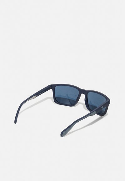Ochelari de soare cu un cadru din plastic mat de culoare albastru marin, lentile pătrate și sticlă colorată în nuanțe de albastru închis. Include brațe drepte cu detalii subtile de branding.