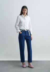 Balta pogātas krekls ar priekšpuses detaļām, zilas taisni griezta stila džinsas un rozā augstpapēžu kurpes. Vienkāršs, tīrs dizains.