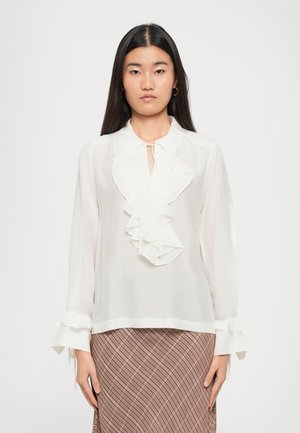White blouse featuring ruffled front, tie closure at neck, and flared cuffs. The fabric appears lightweight and semi-sheer.