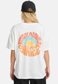 T-shirt bianca in cotone a maniche corte con una grande grafica retro in arancione e blu che presenta immagini di sole e il testo "Pillabong Since 73".