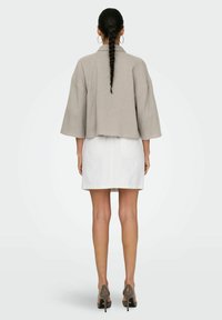 Giacca corta grigia chiara con maniche larghe, tessuto strutturato e colletto, abbinata a una gonna in denim bianca e tacchi beige.