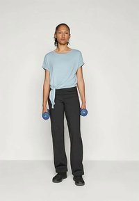 Hele sinine lühikeste varrukatega topp, mille ees on sõlm, koos mustade kitsaste pükste ja mustade kingadega. Inimene hoiab käes siniseid hantleid.