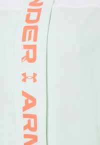 Biała tkanina z pionowym paskiem ozdobionym nazwą marki "Under Armour" i logo w wyraźnych pomarańczowych literach.