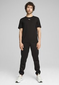 Camiseta negra con un logo sutil, combinada con pantalones deportivos negros. El modelo lleva zapatillas blancas. Tejido suave, ajuste atlético. Diseño simple.
