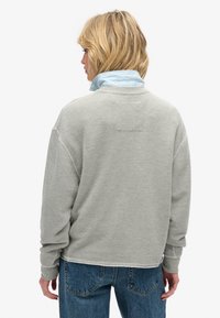 Sudadera gris con un ajuste relajado, que presenta un cuello de canalé y un acabado de costura simple. Combinada con jeans de mezclilla azul, vista desde la parte posterior.