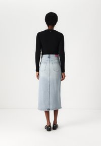 Lys blå denim midi skjørt med rett snitt, to baklommer, og et liv med rosa aksent. Brukt sammen med en svart, ribbestrikket topp med lange ermer.