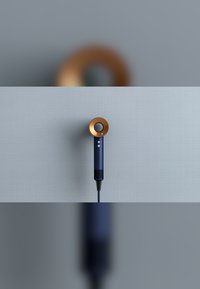 Föhn met een ronde, gouden accent en een donkerblauwe behuizing; heeft knoppen en een getextureerde grip; kabel die uit de basis komt.