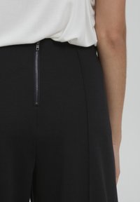 Schwarze Hosen mit einem diskreten Reißverschluss hinten, aus einem glatten Stoff gefertigt, mit einer taillierten Passform und klaren Linien.