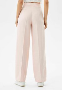 Světlé růžové kalhoty s širokými nohavicemi vyrobené z měkké látky, s vysokým pasem a čistým zakončením na lemu. Nosené s bílými teniskami.