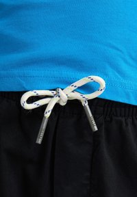 Camiseta de algodón azul con escote redondeado combinada con pantalones cortos negros, que presentan un cordón blanco con acentos azules y verdes y puntas de metal.