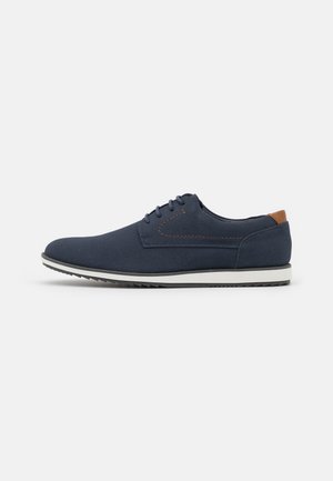 Navy blue lace-up shoes made of textured fabric, featuring a light-colored sole and a brown leather accent on the heel.