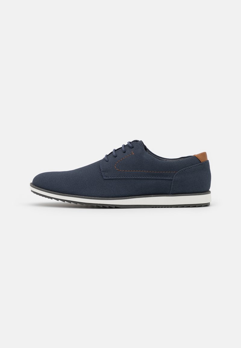 Zapatos de cordones azul marino hechos de un tejido texturizado, con una suela de color claro y un acento de cuero marrón en el talón.