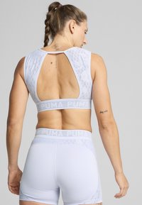 Conjunto de sujetador deportivo blanco y pantalones cortos con un diseño de encaje texturizado, que presenta una espalda con corte y una cinturilla elástica con el logotipo "PUMA".