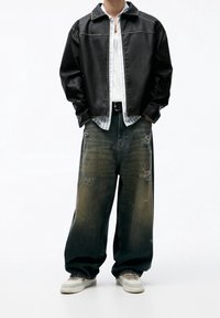 Black leather jacket with light stitching, worn over a striped shirt. Paired with loose-fitting distressed denim jeans and light sneakers.