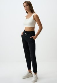 Hellbeige, ärmelloses Cropped-Top mit rundem Halsausschnitt, kombiniert mit schwarzen, elastischen Hosen mit seitlichen Taschen und Kordelzugdetails.