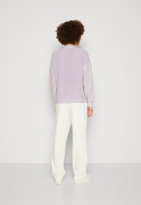 Lila stickad tröja med ribbat mönster, kontrasterande ljusa ärmar och en avslappnad passform, tillsammans med vita vida byxor och plattformsskor.