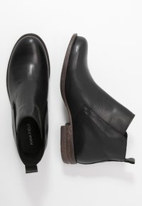 Bottines en cuir noir avec un bout arrondi, des panneaux latéraux élastiques et un talon marron texturé. Finition lisse, détails minimaux.