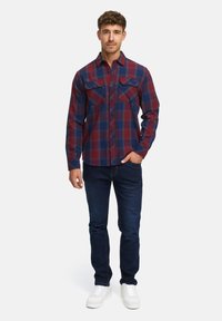 Röd och marinblå rutigt flanellskjorta med långa ärmar och två bröstfickor, i kombination med mörka jeans och vita sneakers.