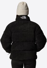 Czarna kurtka puchowa o textured wykończeniu, z wysokim kołnierzem i logo na plecach. Całość dopełnia beanie w kolorze kremowym.