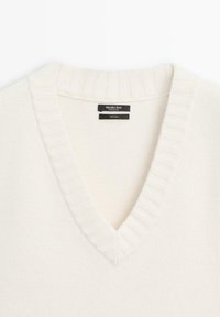 Pull en laine couleur crème avec un col en V côtelé, montrant l'étiquette de la marque "Massimo Dutti" et l'étiquette du tissu à l'intérieur du col.