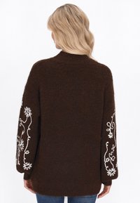Pulover tricotat maro cu guler înalt și mâneci lungi, având broderii florale albe pe mâneci. Material moale, texturat.