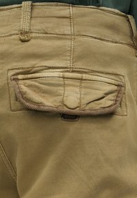 Khakihosen aus strukturiertem Stoff, mit einer großen Klappentasche hinten und kontrastierenden Nähten an den Kanten.