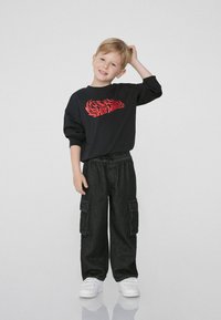 Czarna bluza z kapturem z czerwonym napisem "Hot Wheels", zestawiona z luźnymi, ciemnoniebieskimi spodniami cargo i białymi trampkami.