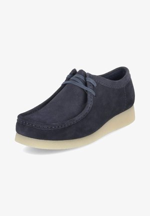 Dark navy suede shoes with a rounded toe, thin laces, and a light-colored rubber sole. Features stitched detailing along the upper.