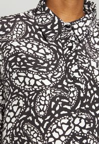 Camisa em preto e branco com um padrão abstrato texturizado, com design de botão e colar clássico. O tecido parece leve e suave.