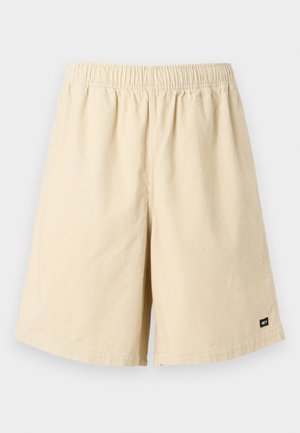 Beige corduroy korte broek met een elastische tailleband en een aangehecht etiket aan de onderkant rechts. De stof heeft een gestructureerd, geribbeld patroon.