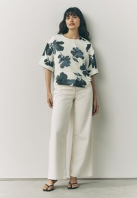 Floral print top in white and dark blue, featuring a relaxed fit and short sleeves, paired with high-waisted, wide-leg cream pants.