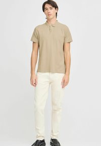 Polo shirt tan con maniche corte, colletto a coste e piccolo logo sul petto. Abbinato a pantaloni bianchi slim-fit e scarpe nere.