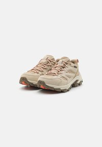Beige fotturer laget av syntetisk materiale med mesh-paneler, oransje detaljer, teksturert såle og forsterket tåhette for holdbarhet.