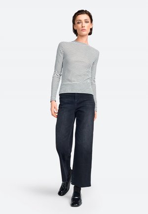 Gestreiftes Langarmshirt in Weiß und Schwarz, kombiniert mit weiten dunklen Jeans. Das Model trägt glänzende schwarze Schuhe. Einfaches, modernes Design.