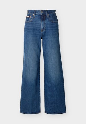 Kék, magas derekú, széles szárú farmernadrág elöl gombos, cipzáras és öt zsebes kivitelben, egyszínű háttér előtt.