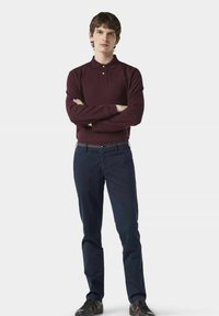 Burgunderfarbendes Langarm-Poloshirt mit Kragen und Drei-Knopf-Leiste, kombiniert mit marineblauen Hosen und schwarzen Sneakers mit roten Akzenten.