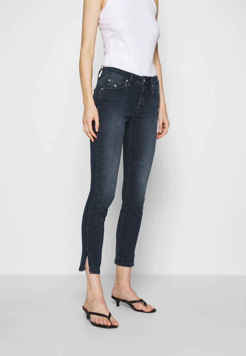 Jeans in denim blu scuro con vestibilità slim, dotati di tasche frontali, fessure laterali alle caviglie e un classico design a cinque tasche.