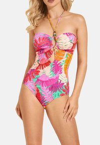 Kolorowy jednoczęściowy strój kąpielowy w stylu bandeau, z wycięciami i intensywnymi wzorami tropikalnych liści w odcieniach różu, zieleni i pomarańczy.
