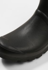 Bota de borracha preta com bico arredondado, superfície texturizada e sola padronizada para melhor aderência. Projetada para proteção à prova d'água e durabilidade.