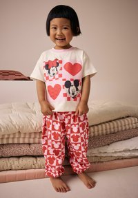 Bílý tričko s grafikou Minnie a Mickey Mouse v červených srdcích; červené a růžové vzorované kalhoty se siluetami Mickey Mouse.