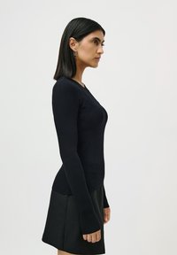 Tricou negru cu maneci lungi, cu un siluetă ajustată, având un decolteu rotund și manșete extinse. Asortat cu o fustă texturată neagră.