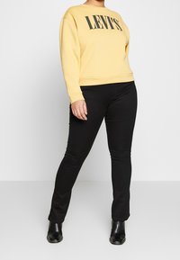 Sudadera amarilla con el texto negro "LEVI'S", combinada con jeans negros ajustados y botas de tobillo. Diseño sencillo, colores sólidos y ajuste casual.