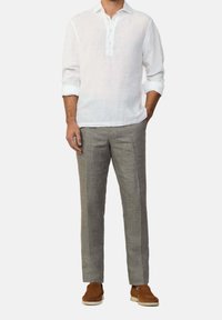 Camicia di lino bianca con abbottonatura a mezza patta, abbinata a pantaloni di lino grigio chiaro e scarpe in suede marrone. Vestibilità casual e rilassata.