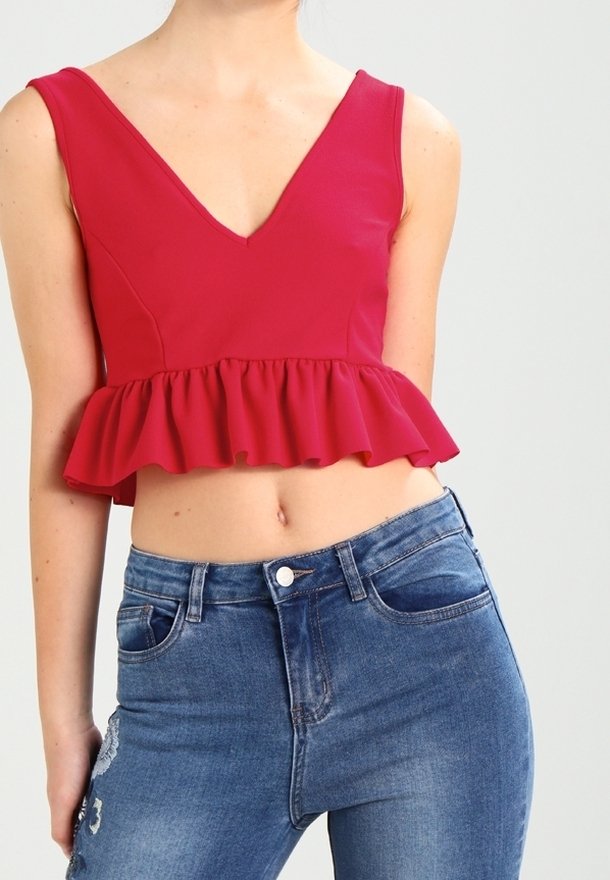 Top peplum rosso con scollo a V profondo, realizzato in tessuto morbido. Abbinato a jeans blu con una vestibilità aderente e delicati dettagli decorativi.