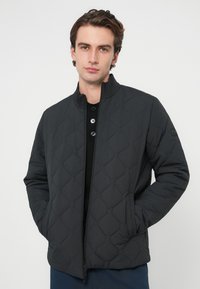 Czarna pikowana kurtka z wysokim kołnierzem, przednim zamkiem błyskawicznym i dwoma bocznymi kieszeniami. Tkanina ma gładką fakturę i geometryczny wzór na całej powierzchni.