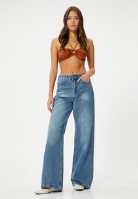 Brun cropped top med twist-detajle og cirkulært accent, parret med brede lyseblå jeans med høj talje og subtil falming.