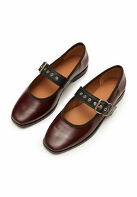 Zapatos de cuero burdeos con puntera cuadrada, correa negra al tobillo con hebilla plateada y agujeros decorativos, textura suave, tacón bajo.